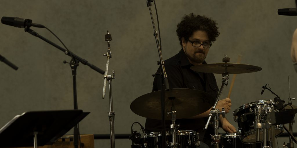Image of David T. Little playing the drums and making a face